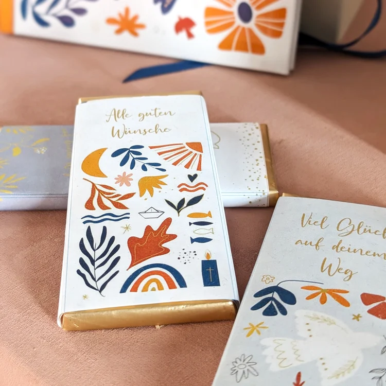 Zwei Schokoladentafeln und GEschenkbücher mit braunen und blauen Motiven auf einem Tisch.
