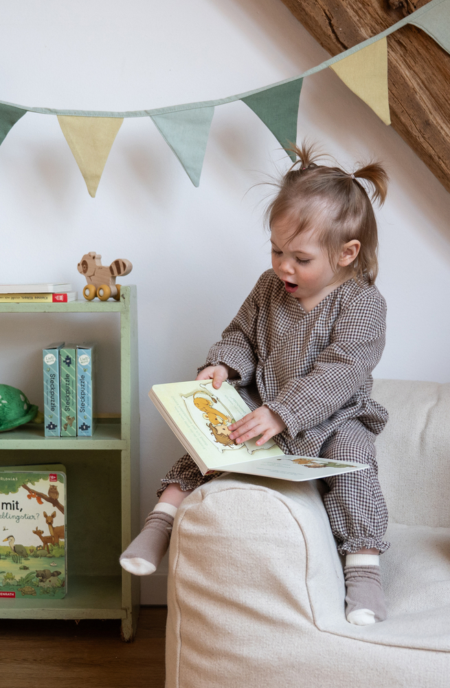 Foto eines kleinen Kindes in kariertem Overall, das auf einem Sofa sitzt und Schieber in einem Kinderbuch betätigt.