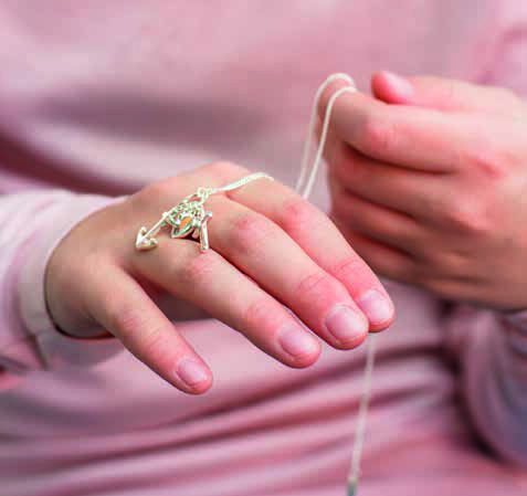 Eine silberne Kette mit einem Anker und einem Kreuz liegt auf dem Handrücken eines Kindes.