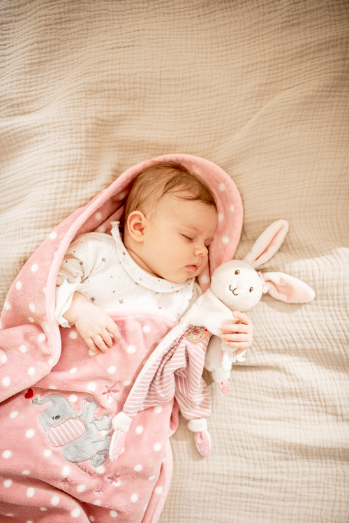 friedlich schlafendes Baby auf einer rosa Plüschdecke mit einem Kuschelhäschen im Arm