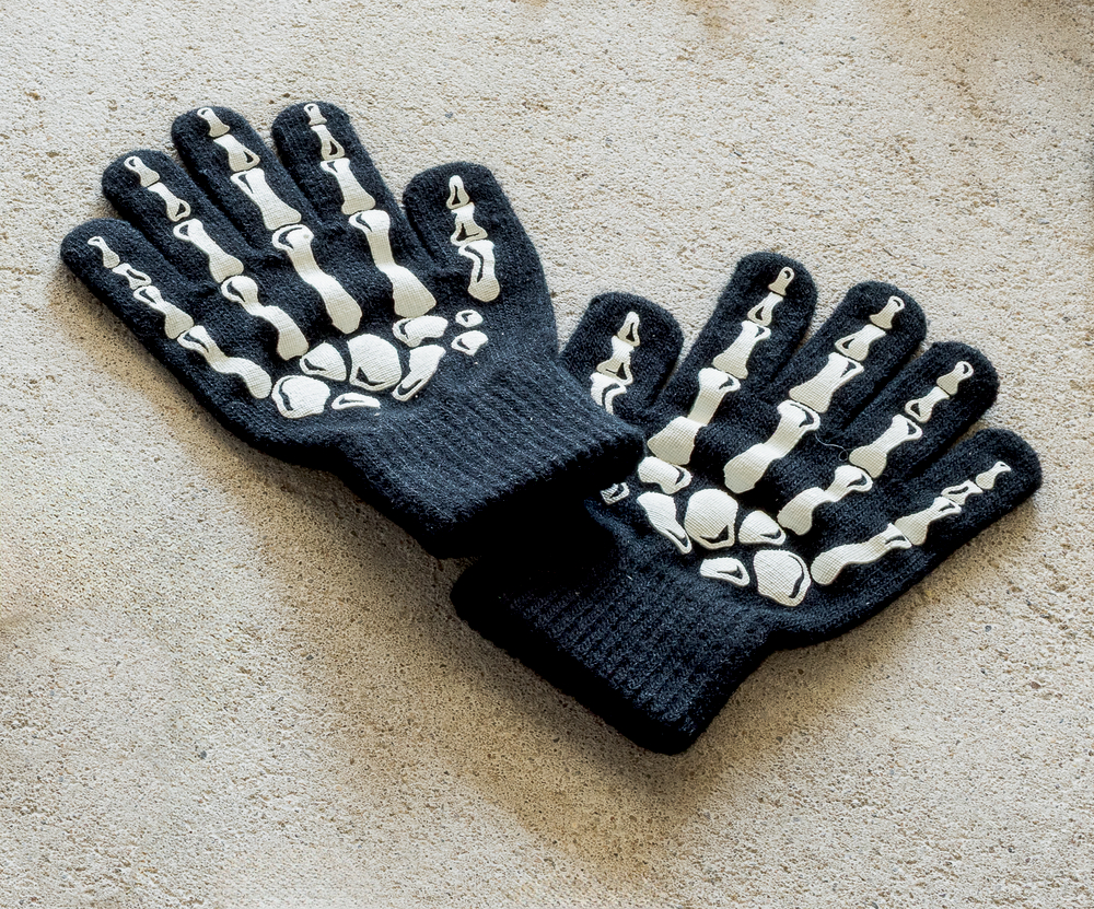 Schwarze Strickhandschuhe mit weißen Skelettknochenmotiven auf der Oberseite.