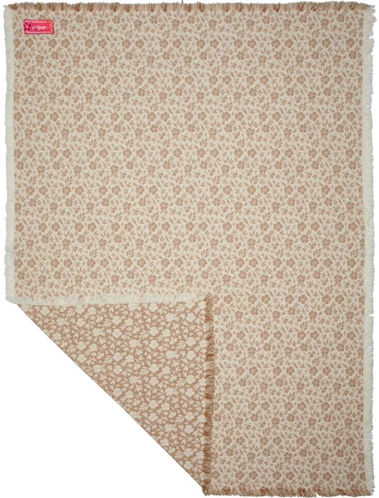 Beige Decke mit Blumenmuster und ausgefransten Rändern, eine Ecke ist gefaltet, sodass die Rückseite sichtbar ist.