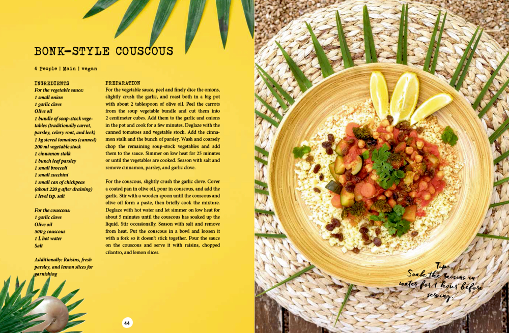 Couscous mit Kichererbsen und Gemüse, garniert mit Zitronenspalten und Kräutern, serviert auf einer gewebten Matte.