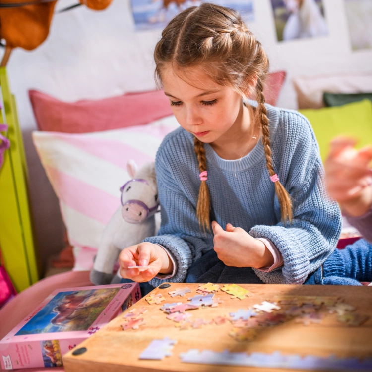 Ein Mädchen an einem Tisch in einem Kinderzimmer ist ins Puzzeln vertieft.