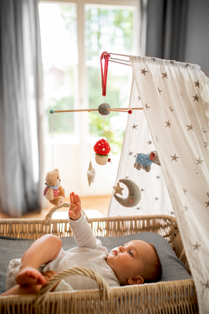 Ein Baby in einem Kinderbett greift nach einem Plüschmobile, das unter einem Himmel mit Sternenmuster hängt.