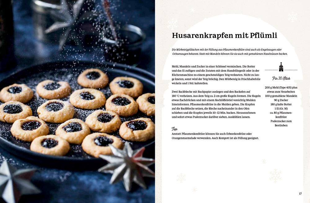 Puderzucker wird von Hand über mit Marmelade gefüllte Plätzchen auf einem Backblech gestreut.