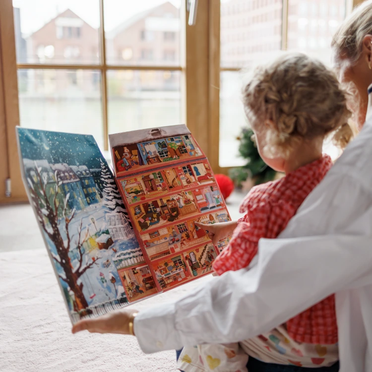 Frau und Mädchen betrachten ein winterliches Buch in Hausform.