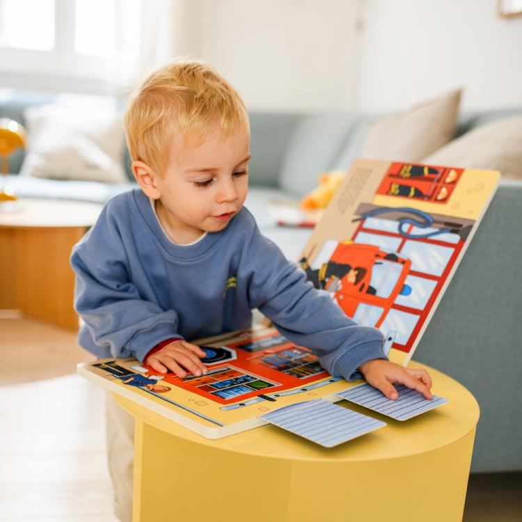Kleiner Junge probiert die Klappen eines Pappbilderbuchs aus.