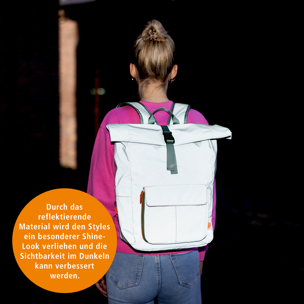 Person mit hellgrauem Rucksack mit reflektierendem Material, von hinten gesehen, trägt pinken Pullover und Jeans.