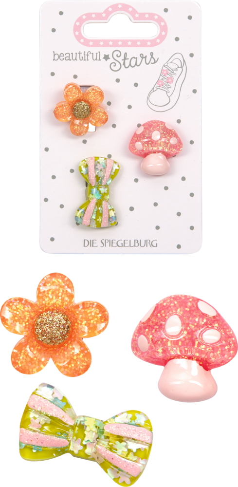 Drei glitzernde Sneaker Charms in Form von Blume, Fliegenpilz und Schleife, dahinter noch mal die Verpackteansicht, auf Karton mit Punkten.