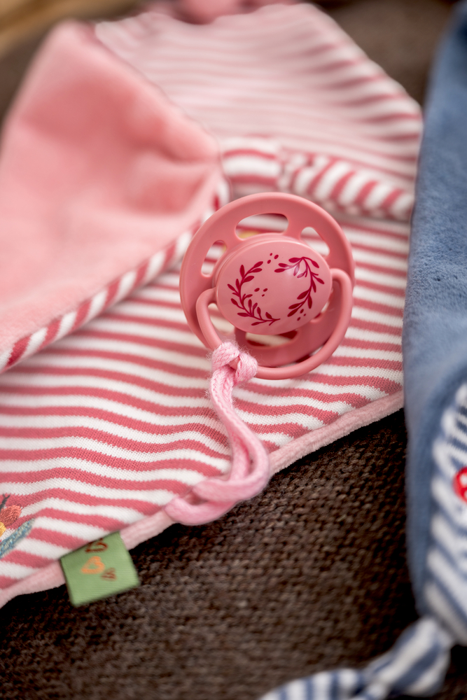 Rosa Schnuller mit floraler Verzierung auf rosa-weiß gestreiftem Schnullertuch mit angenähter Kordel.