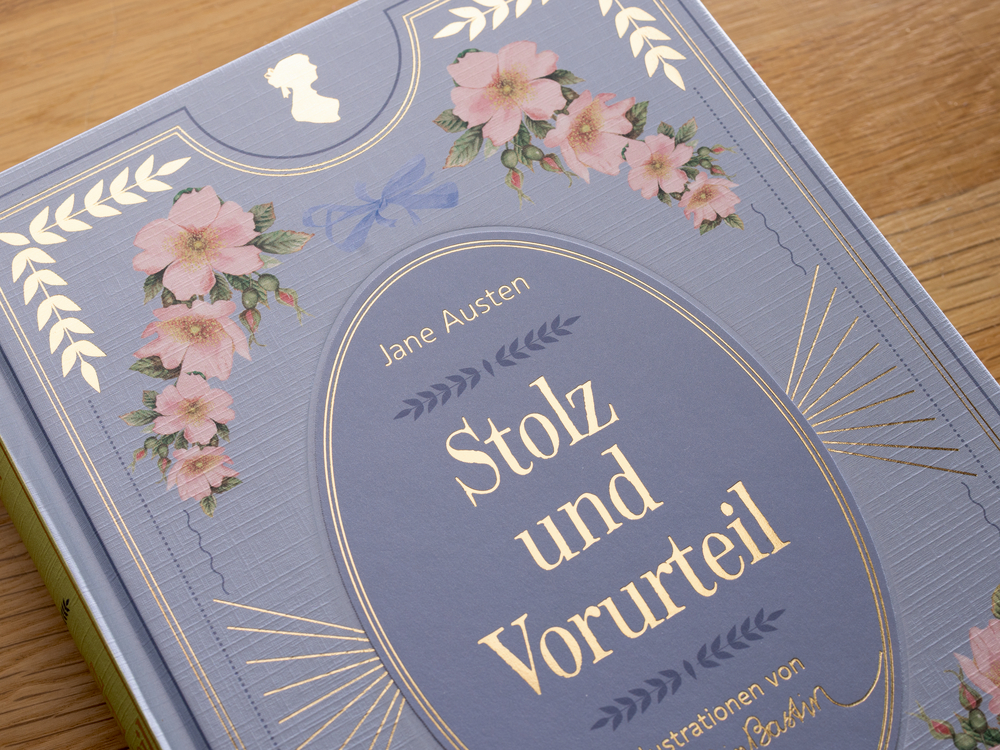 Helblaues, verziertes Buchcover mit goldener Schrift auf einem Tisch.