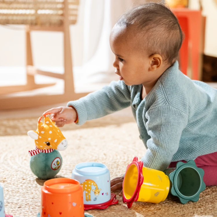 Baby spielt mit Stehauf-Giraffe und Stapelbechern.