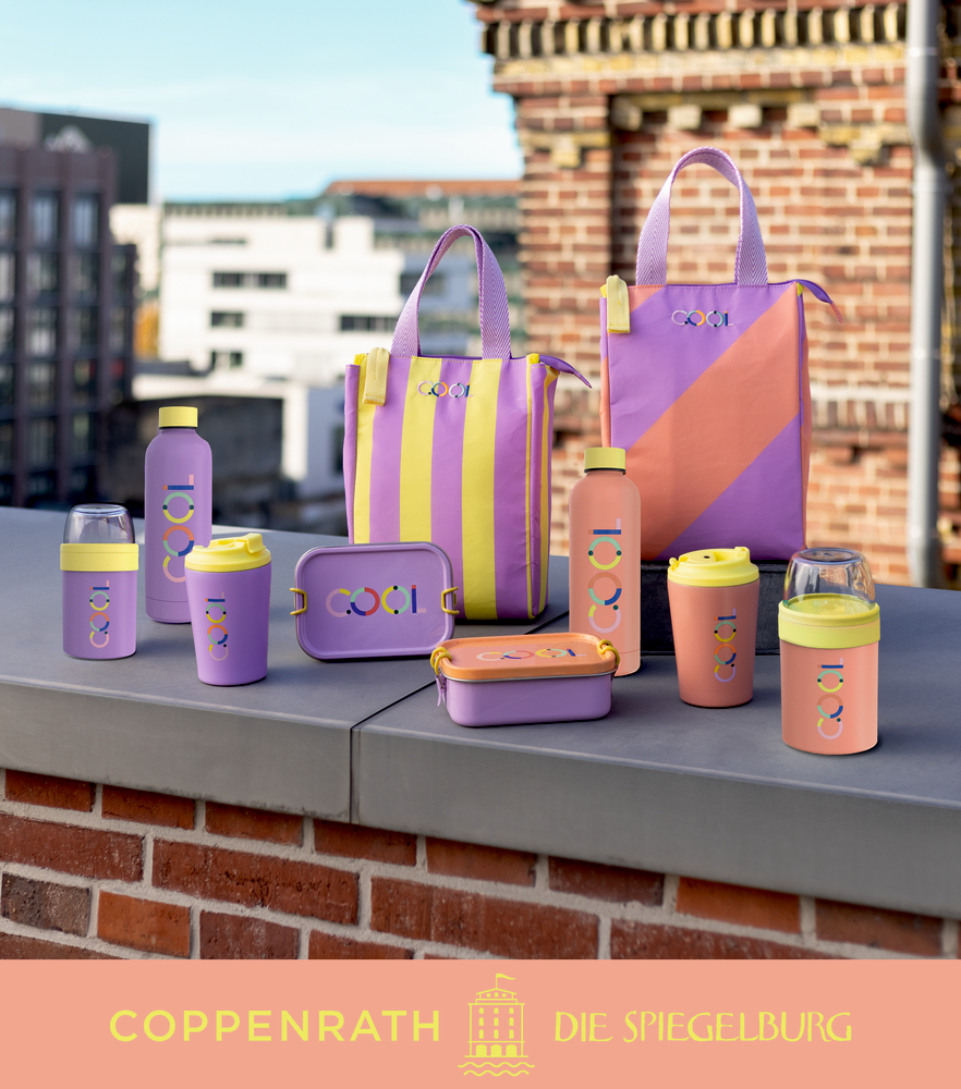 Pastellfarbene Trinkgefäße, Lunchboxen und Taschen, präsentiert auf einem Dach mit der Skyline einer Stadt im Hintergrund.