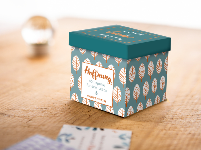 türkise Box mit orange, weißen Blättern und orangener Aufschrift Hoffnung auf einem Holztisch