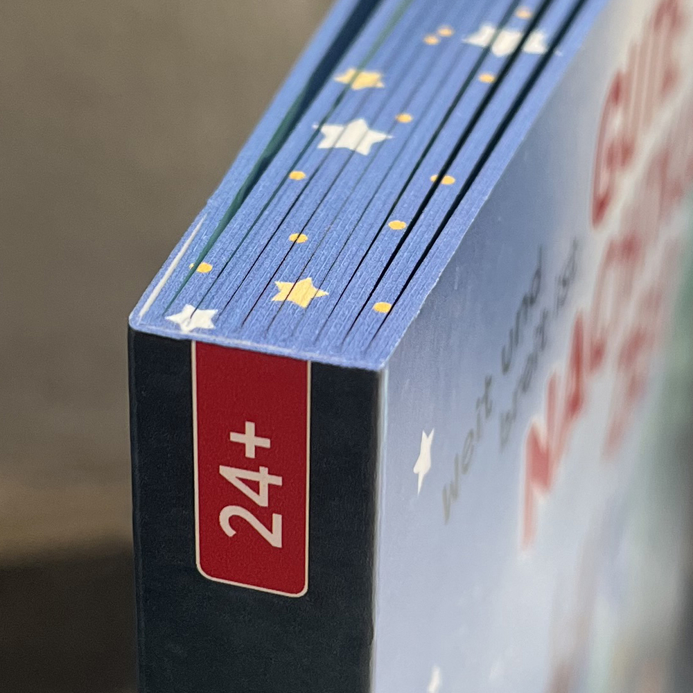 Nahaufnahme einer Kartonkante mit blauem Sternenmuster und rotem Feld mit weißer Aufschrift „24+“.