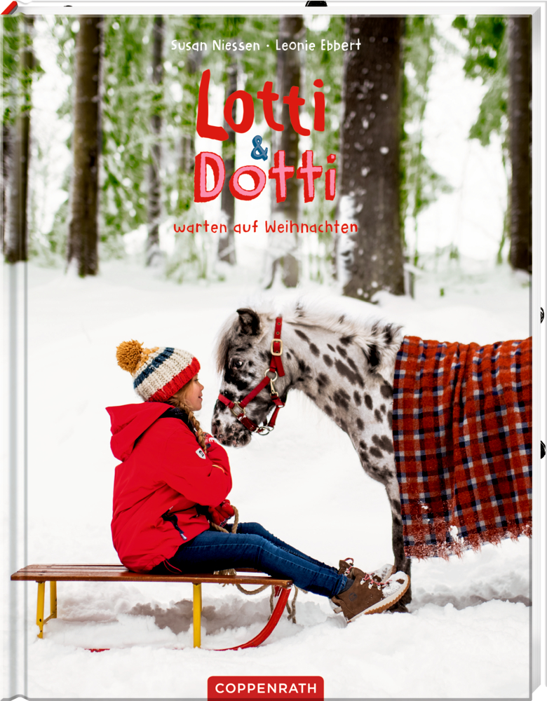 Ein Mädchen in Rot sitzt auf einem Schlitten vor einem Pony mit Plaid-Decke im verschneiten Wald.