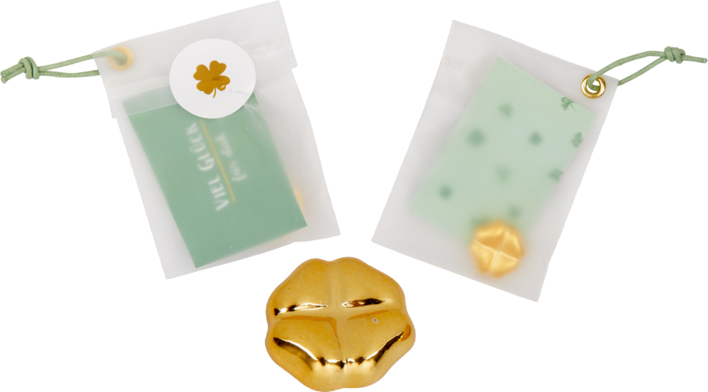 Kleines goldenes Kleeblatt und zwei durchsichtige Tütchen mit farbigem Band, kleinen Kärtchen und winzigem goldenen Kleeblatt im Inneren.