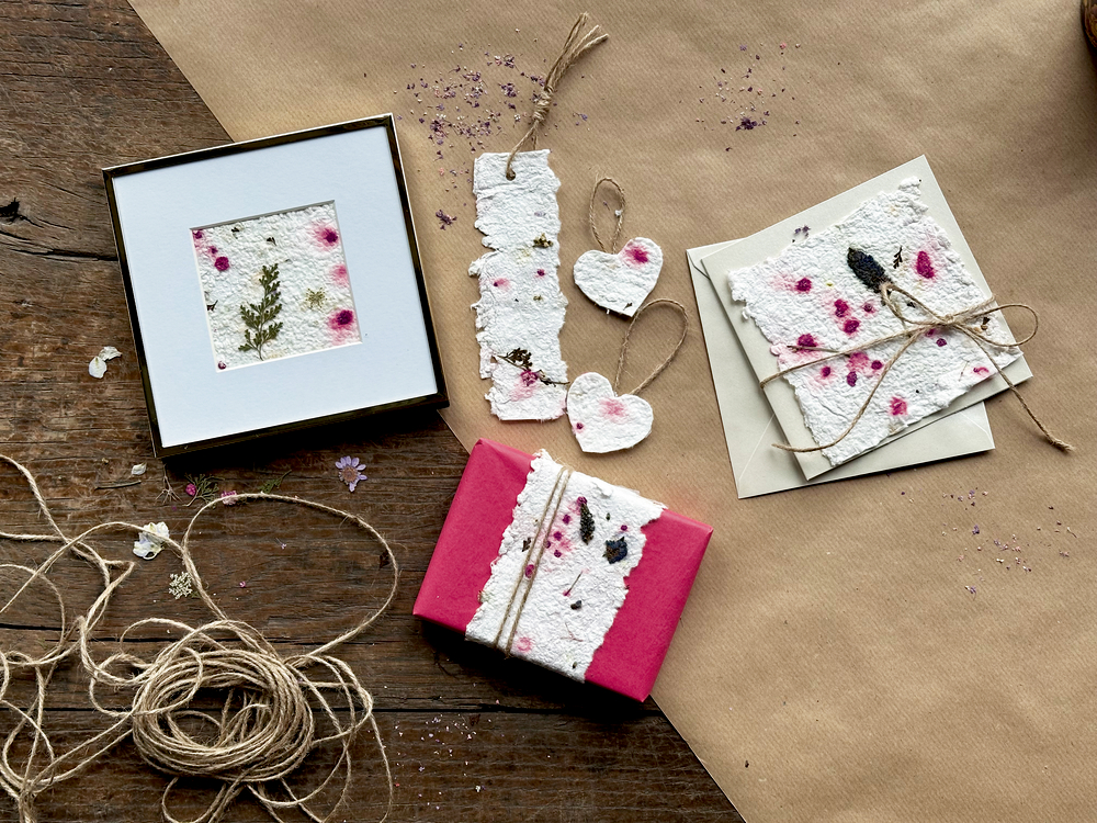 Papierkarten, Anhänger und Geschenke mit getrockneten Blumen und Kordel auf Holztisch.