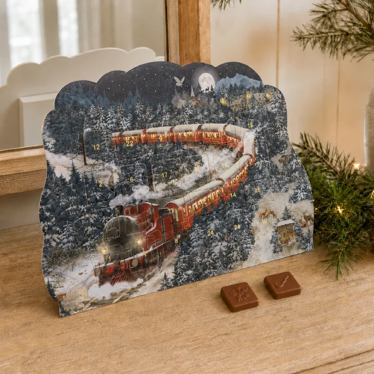 Kleiner Kalender mit nostalgischer Eisenbahn auf einer Kommode. Dazu Zweige und 2 SChokostücke.