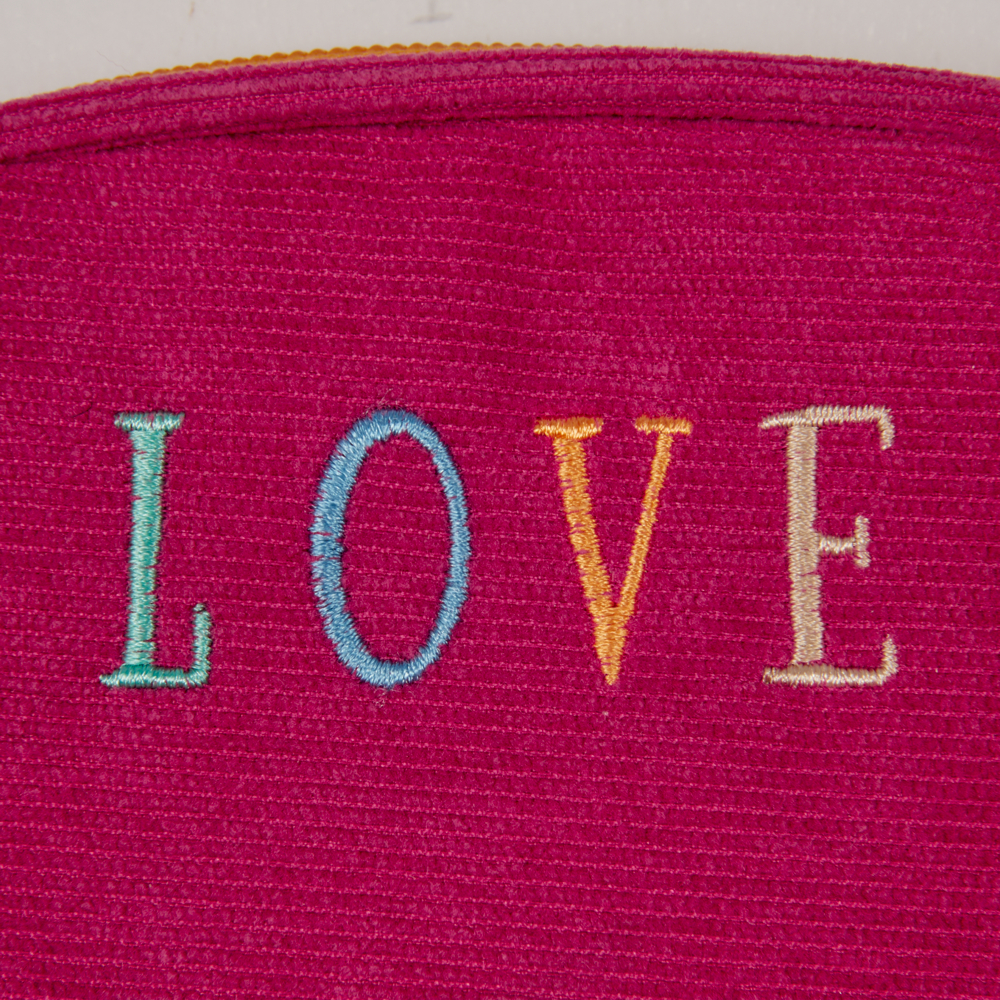 „LOVE“ in bunten Buchstaben auf strukturierten pinken Stoff gestickt.