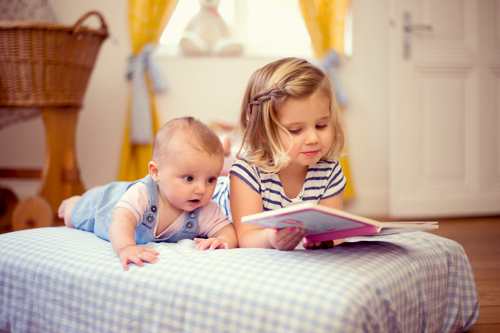 Foto: Zwei Kinder liegen im Bett, das ältere liest dem jüngeren ein Buch vor.