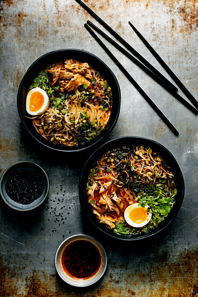 Zwei Ramen-Schüsseln mit Eiern, zerkleinertem Fleisch, Kräutern und Essstäbchen auf einer rustikalen Metalloberfläche.