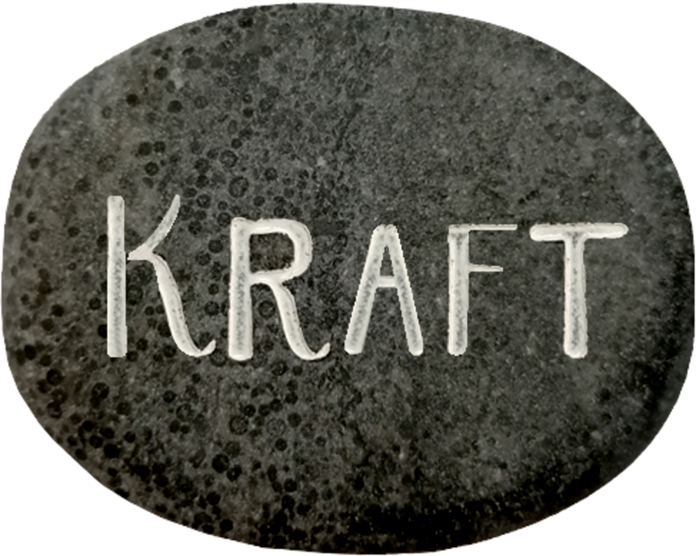 Ein dunkler Stein mit der Gravur „KRAFT“ in weißen Großbuchstaben.