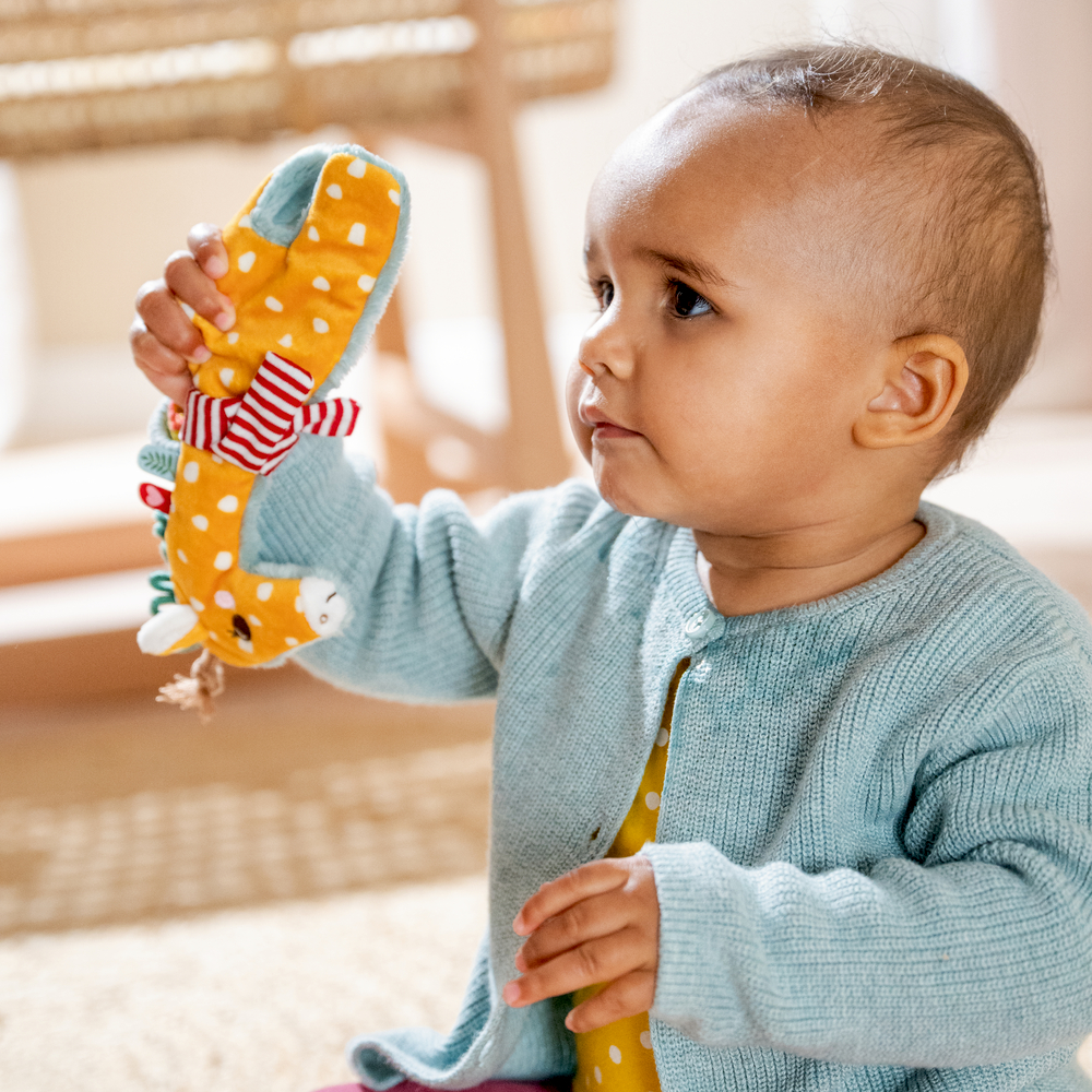 Ein Baby im blauen Pullover hält ein buntes Plüschtier in Giraffenform.