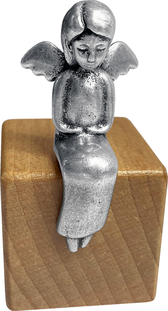 Eine metallene Engelsfigur mit Flügeln sitzt auf der Kante eines Holzblocks und blickt nach unten.
